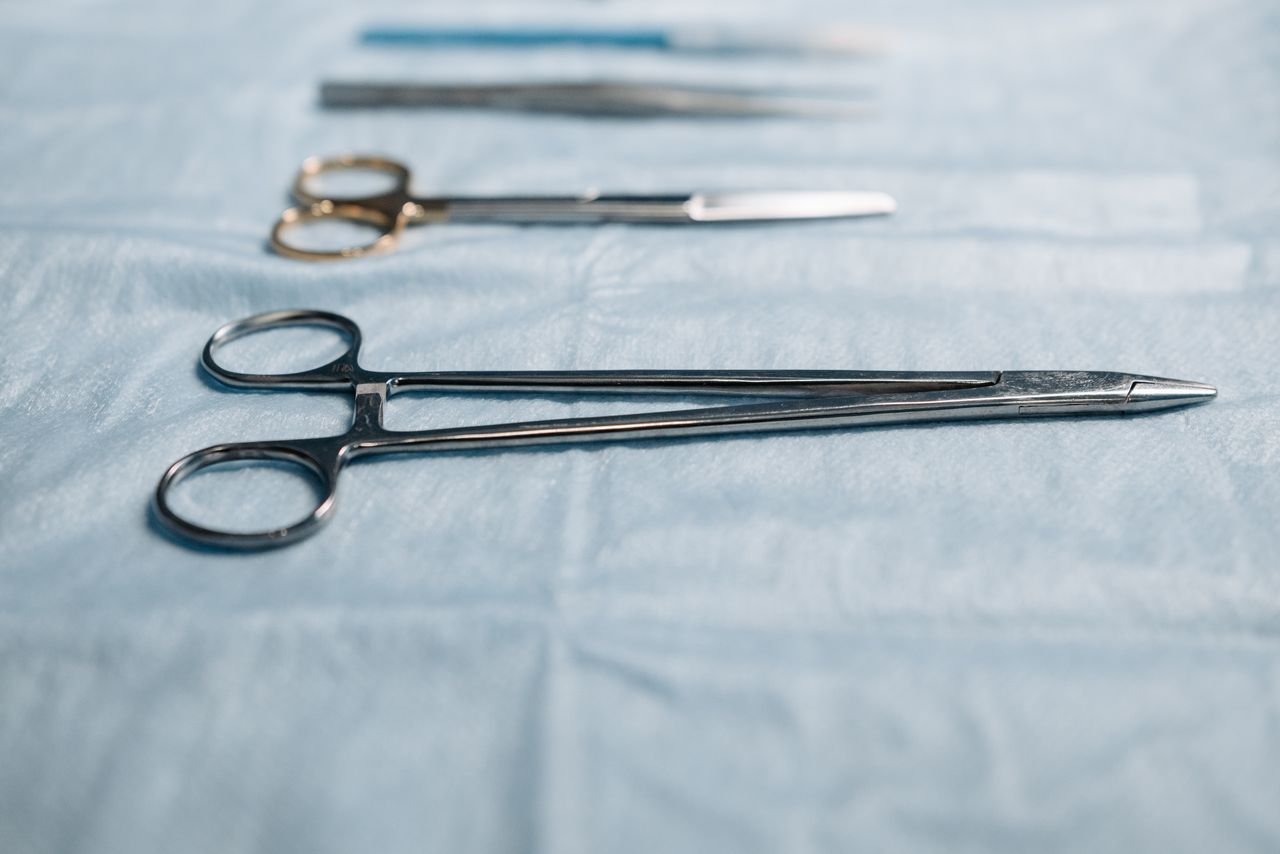 heros-img Close-up of surgical tools including a needle holder on a blue cloth in a medical setting.